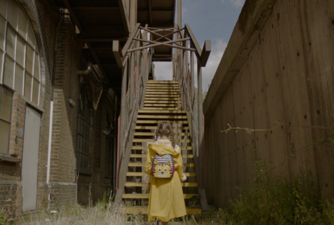 A young person wearing yellow looking up at a flight of stairs on an abandoned house.