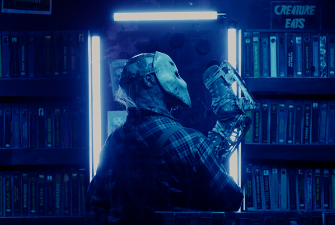 Person wearing a hockey mask, holding an ice skate, inside a video store.