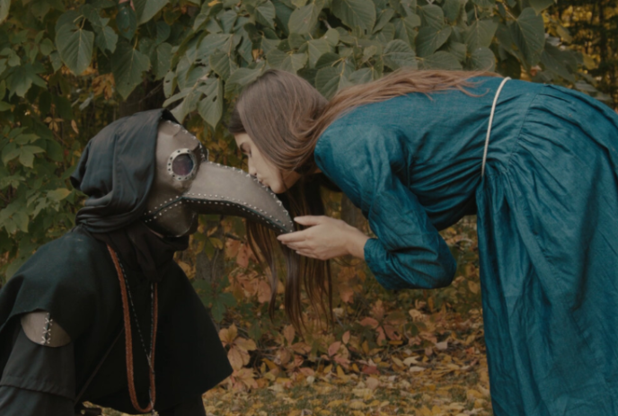 A person bending down and kissing the nose of a person wearing a plague doctor outfit.