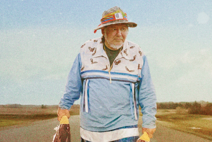 Indigenous person walking along a road with feathers in their hands.