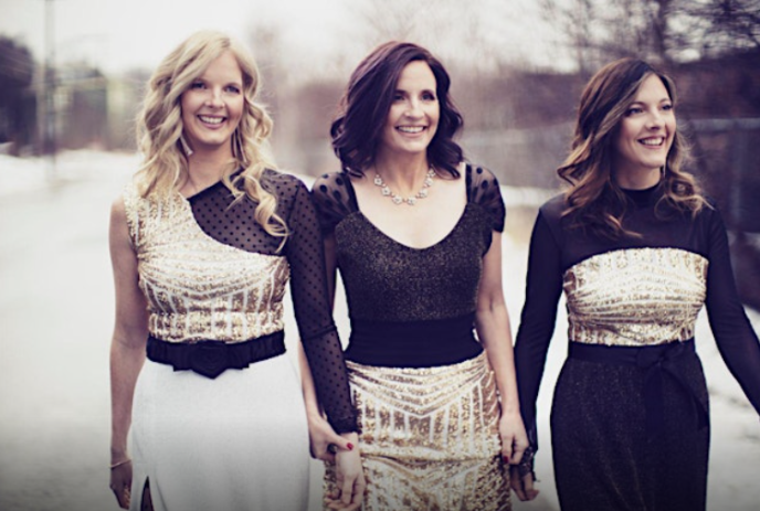 The three Ennis Sisters, dressed in black and gold, walking along a road together.