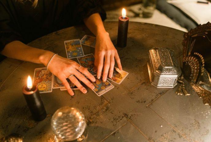 A dark psychic atmosphere with a person handling cards, a crystal ball, lighted candles and a silver box.