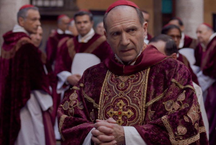 Person dressed as a Cardinal with other Cardinals around them, looking distressed.