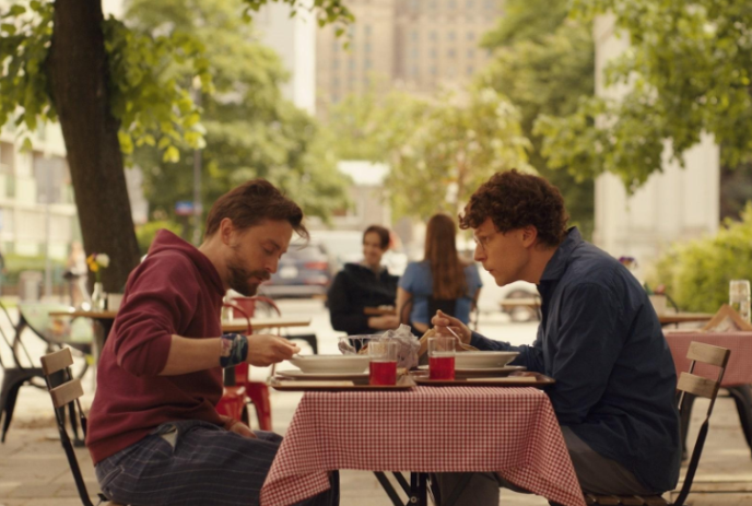 Two people sitting at a table outside eating.