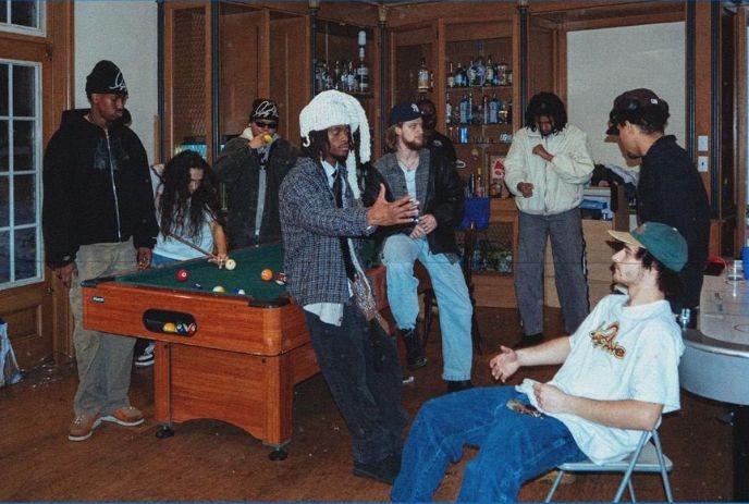 A group of people gathered in a room with wooden cabinets filled with bottles.