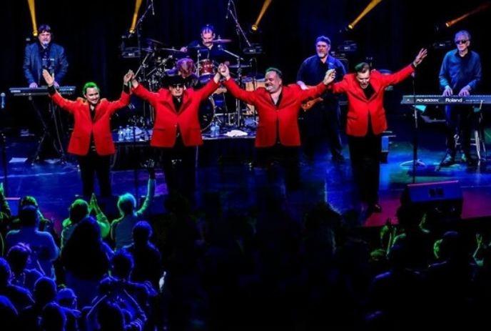 Four male band members from Jersey Nights performing on stage giving a bow, wearing red jackets.