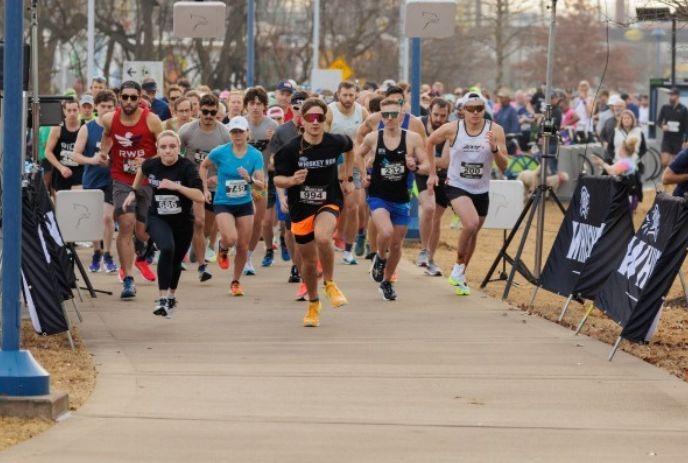 Group of runners participating in a race, wearing athletic gear with trees and spectators in the background.