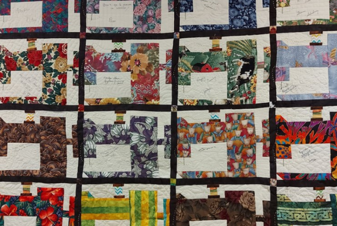 A colourful quilt with different squares hanging on a wall.