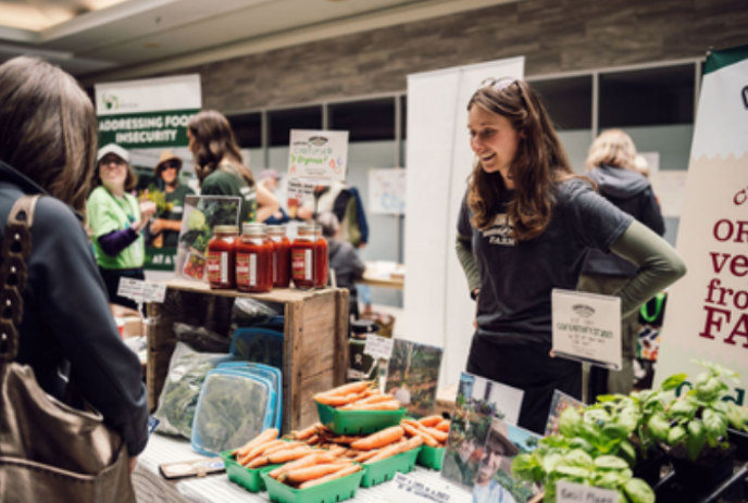 One person standing at a booth selling vegetables to people walking by.