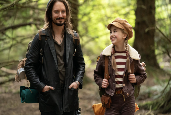 A parent and child walk together in the woods.