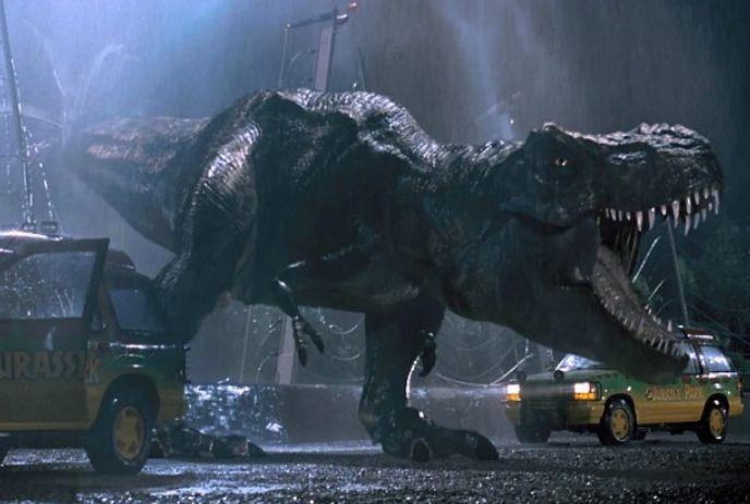 A roaring T-rex stands near a “Jurassic Park” car in the rain, creating a dramatic and tense scene from the movie.