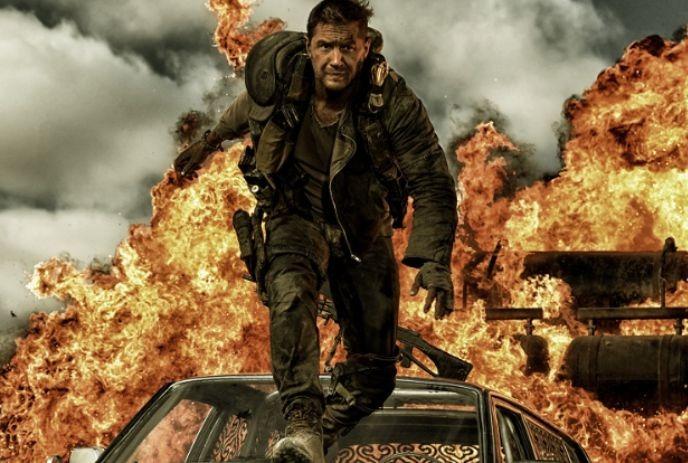 A man in rugged attire jumps off a vehicle while an explosion erupts in the background, surrounded by smoke and flames.