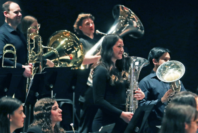 A group of musicians playing brass instruments, including tubas and trombones, during a performance.