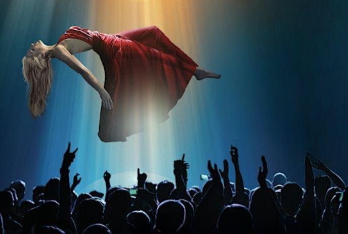 Depicts a woman in a red dress seemingly floating above a crowd under a spotlight.