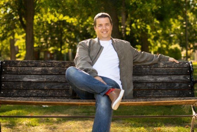 A person sits cross-legged on a park bench with smiling face, surrounded by lush greenery, enjoying a peaceful moment.