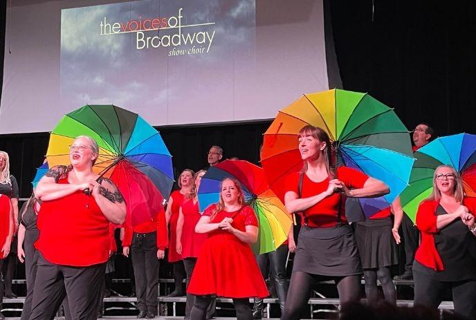 A group of performers, part of 'The Voices of Broadway Show Choir,' holding colorful umbrellas and wearing their costume.