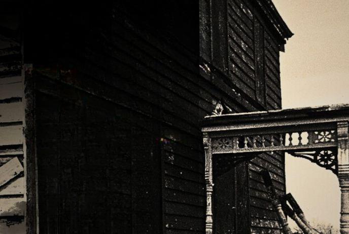 Sepia-toned image of an old, weathered wooden house with intricate details on the porch railing. The Abandoned Village