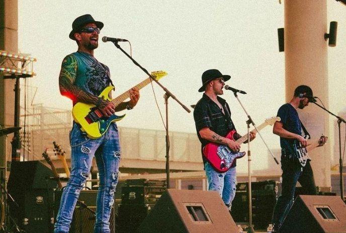 Three men wearing hats perform on stage, each playing a guitar, creating a lively musical atmospher.