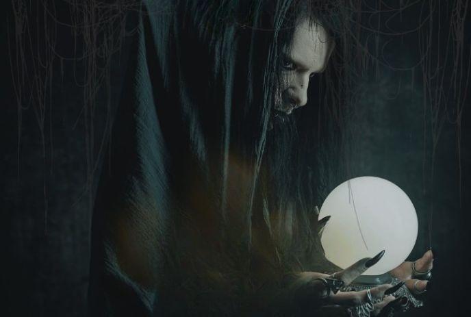 A witch-like figure, cloaked in black, holds a glowing white crystal ball under a dark, radiating an aura of mystery magic.