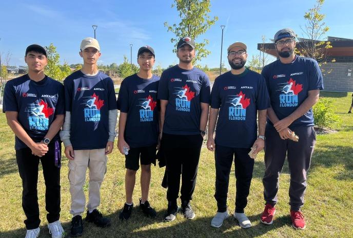 A group of six young men stands outdoors in a park, all wearing matching navy blue 'Run for London' T-shirts.