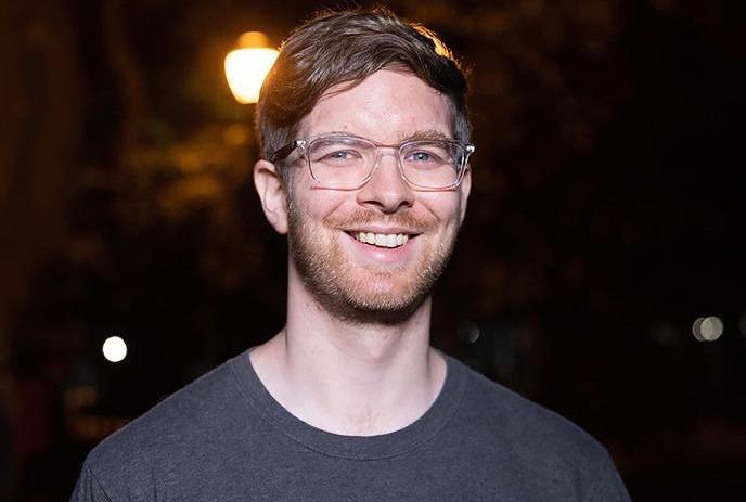 A man wearing glasses and smiling in a party setting, wearing an old Wild N' Restless shirt.