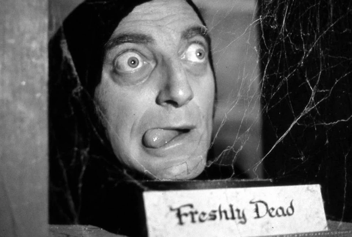 A grayscale image of a blurred object with a label reading “Freshly Dead” in front of cobwebs, creating a spooky atmosphere.