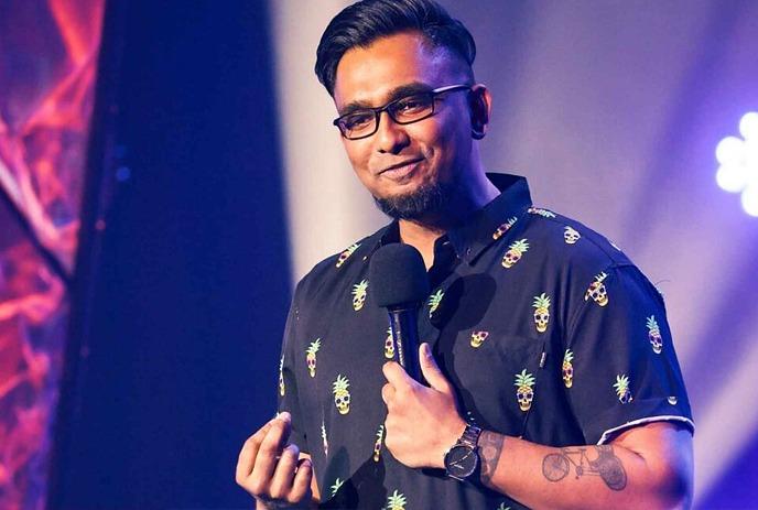 Danish Anwar performing comedy on stage with a microphone in his hand.