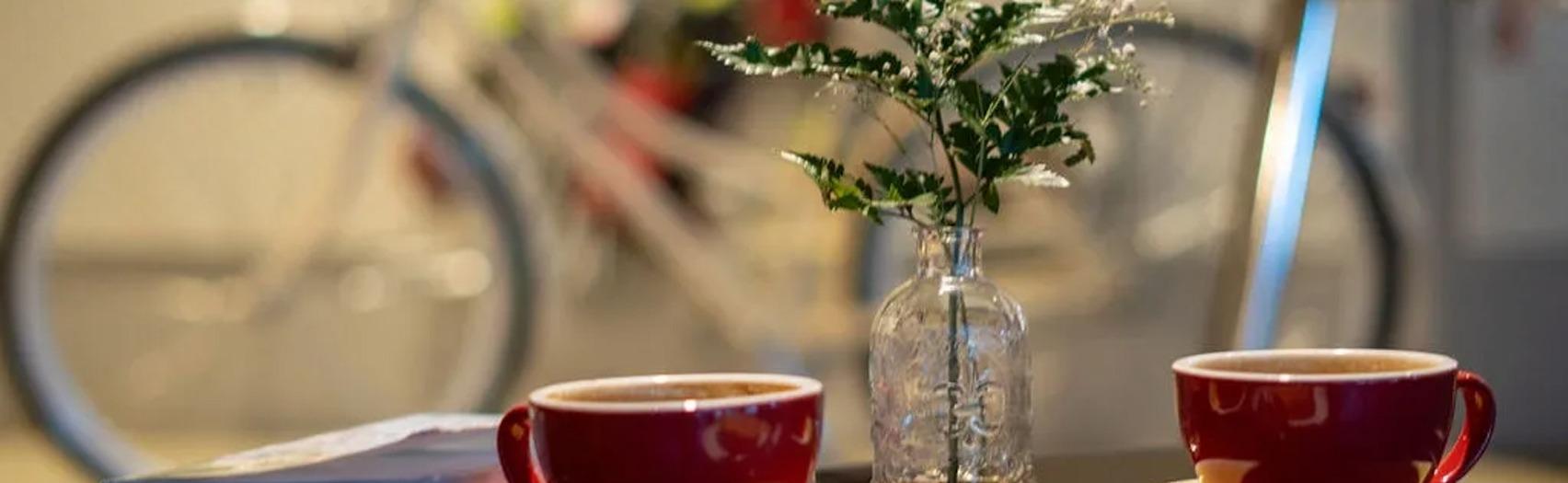 Two coffee cups on a table with books and a flower