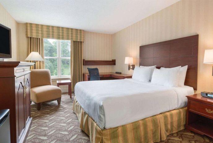 A hotel room with a large bed, desk, chair, and window with curtains, showcasing comfortable, modern amenities.