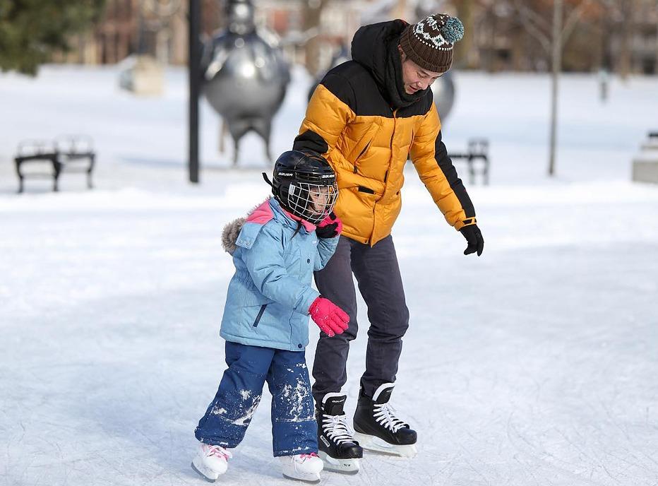 A father and his daughter skating outdoors in Victoria Park locate din London, Ontario