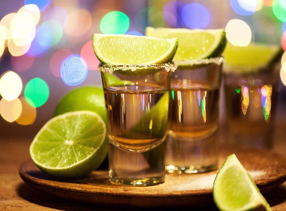 Two shot glasses filled with tequila, rimmed with salt and wedges of limes beside the glasses