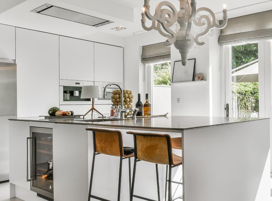 A modern white kitchen setting with an island, wooden stools and a light fixture