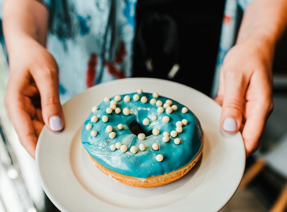 A women holding a colourful donut on a plate from Happiness Cafe located in London, Ontario