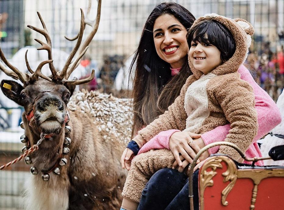 A mother and her child sitting on a red sleigh with a reindeer in the background