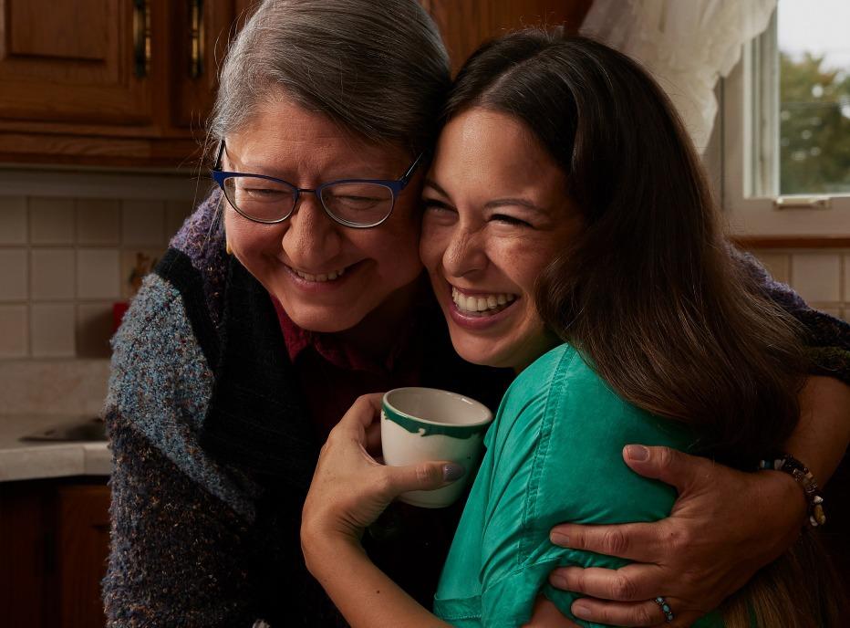 A female hugging her grandmother with a cup of tea in her hand