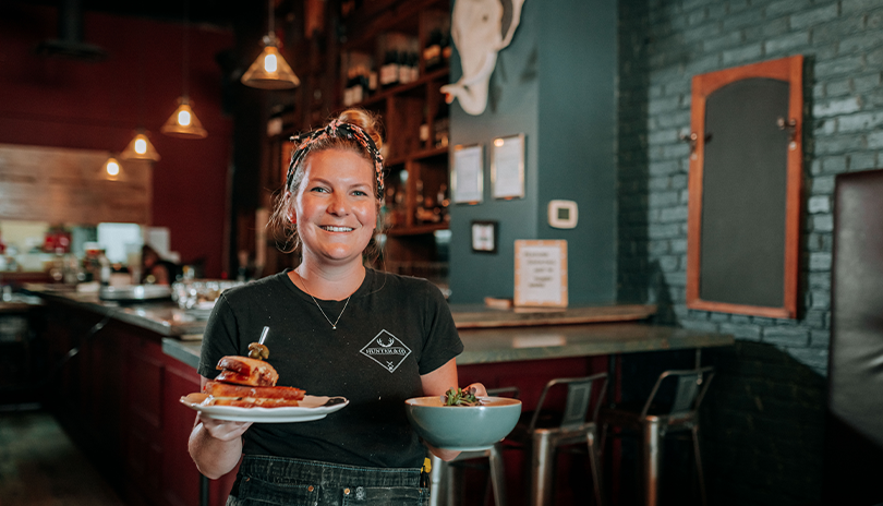 Server smiling with two warm dishes at the restaurant Hunter and Co