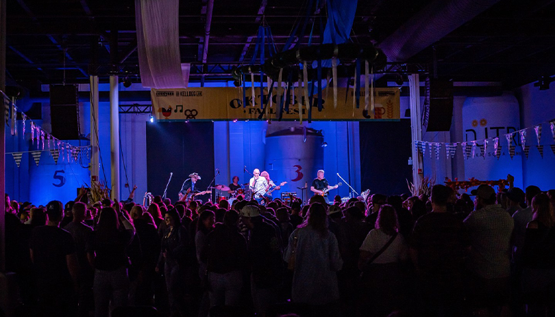 Band performing to an energetic crowd at 100 Kellogg Lane, with beer kegs behind them