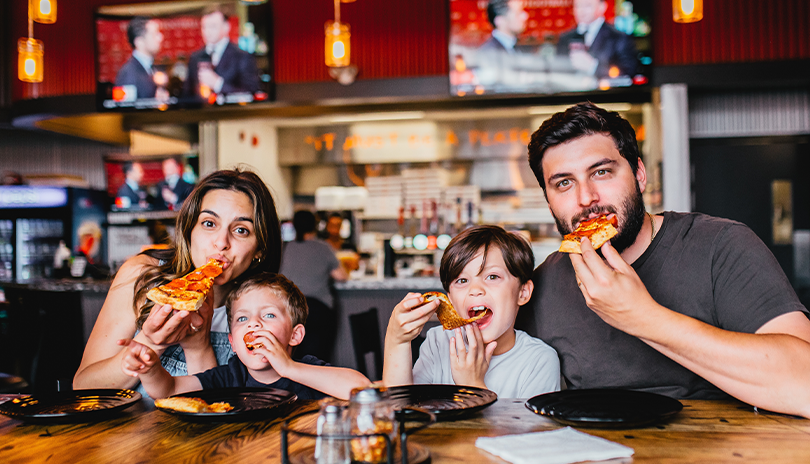 A happy family with children sitting at a table and enjoying pizza in Pizza Projekt located in London, Ontario